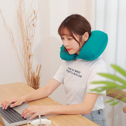 A woman using the green press-inflatable neck pillow while working on a laptop